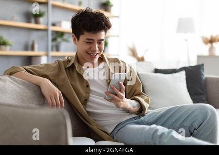 Nahaufnahme eines lächelnden asiatischen Mannes mit Smartphone zu Hause Stockfoto