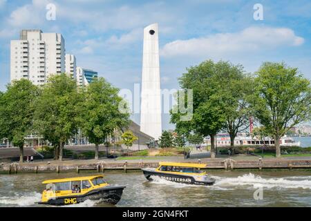 Rotterdam Niederlande - 23 2017. August; Wassertaxis kreuzen auf dem Fluss New Mause durch die Stadt mit einem hohen weißen Kriegs-Gedächtnisturm und einem nahe gelegenen Apartment Stockfoto