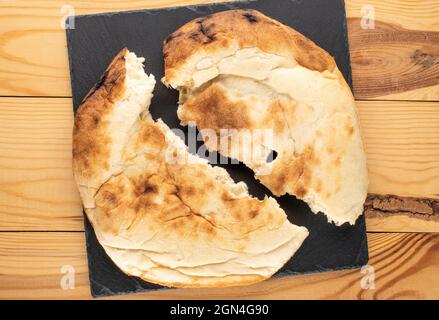 Zwei Hälften frisch gebackener Pita auf einem Schieferstein auf einem Holztisch, Nahaufnahme, Draufsicht. Stockfoto