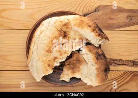 Zwei Hälften frisch gebackenes Pitabrot auf einer Tonplatte auf einem Holztisch, Nahaufnahme, Draufsicht. Stockfoto