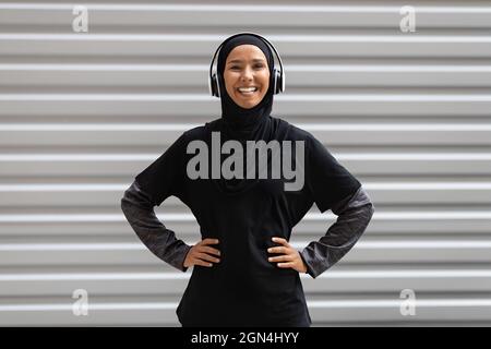 Outdoor-Training. Porträt Einer Sportlichen Muslimischen Frau In Hijab Und Kabellosen Kopfhörern Stockfoto