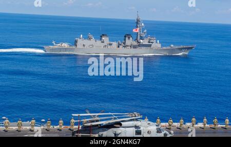 Seeleute der US-Marine an Bord des Flugzeugträgers USS Carl Vinson der Nimitz-Klasse grüßen den Zerstörer JS Ikazuchi der japanischen Maritime Self-Defense Force Murashame-Klasse, der während gemeinsamer Einsätze am 19. September 2021 in der philippinischen See an der Seite vorbeikommt. Stockfoto