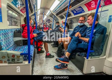 London, Großbritannien. September 2021. Sportlehrer begleiten ihre Schüler auf der U-Bahn, aber sie können trotz des Schildes über ihnen kein Beispiel für das Tragen der Maske geben.der Mann rechts zieht beim ein- und Aussteigen kurz seine Maske an, was darauf hinweist, dass er nicht ausgenommen war - die Maskenverwirrung geht im Untergrund weiter. Die Röhre ist voller und Masken sind immer noch obligatorisch, aber immer mehr Zahlen ignorieren die Anweisungen, die von gemischten Botschaften der Regierung angeführt werden. Kredit: Guy Bell/Alamy Live Nachrichten Stockfoto