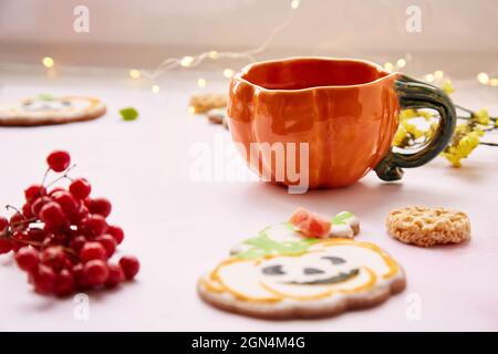 Halloween Kreativkonzept: Kürbisbecher und süße Kekse in Form von festlichen Kürbissen. Stimmungsvolle, ästhetische Herbststimmung oder Trick or Treat-Konzept. Viburnum und kandierte Obstdekorationen. Stockfoto