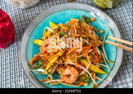Vietnamesischer süßer und saurer Mangosalat mit Garnelen, gebratenen Zwiebeln und Gemüsesprossen auf blauem Teller auf dem Tisch, Essstäbchen. Stockfoto