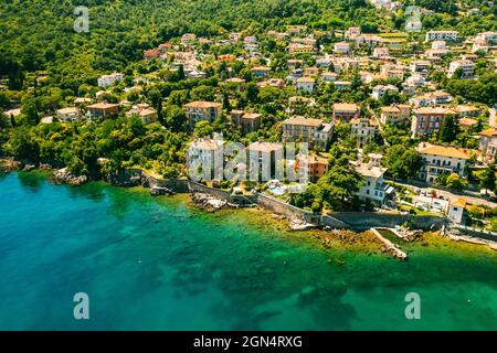 Schöne Villen in der Nähe der Küste von felsigen Strand in einer kleinen Stadt Lovran, Kroatien. Arial Blick auf Lungomare Meer Gehweg mit transparentem Wasser. Stockfoto