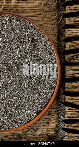 chia-Samen (Salvia hispanica) in einer Tonschale auf einem Holzbrett Draufsicht. Superfood und gesundes Frühstück vertikales Konzept aus der Nähe Stockfoto