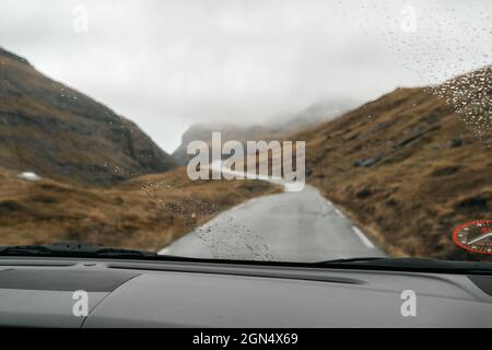 Fahren auf den Färöer Inseln. Skandinavische Natur, braune Felder und Hügel, launischer Himmel Stockfoto