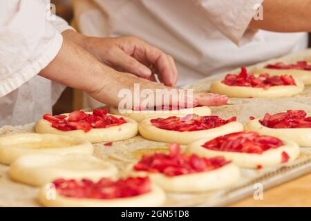 Die Frau auf dem Bild macht gefüllte Obstkuchen. Hände füllen Kuchen Hefeteig mit Erdbeeren. Arbeiten Sie in der Bäckerei. Stockfoto