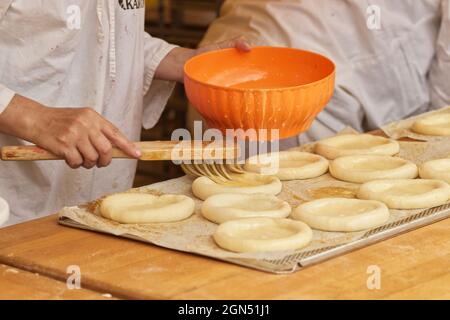 Die Frau auf dem Bild macht gefüllte Kuchen. Hände, die Schutzhandschuhe tragen, beschichten den Pie-Teig mit rohem Ei. Arbeiten Sie in der Bäckerei. Stockfoto