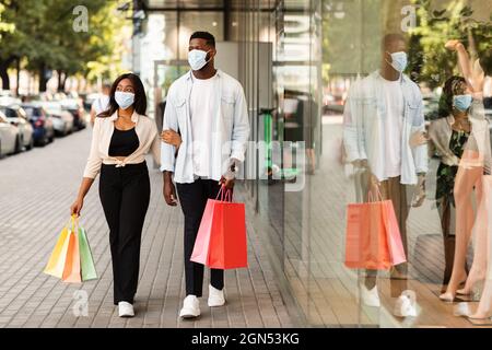 Porträt eines schwarzen Paares in Masken, das mit Einkaufstaschen läuft Stockfoto