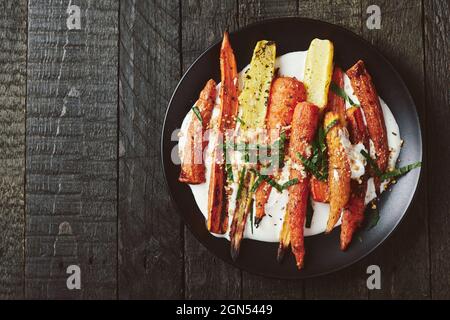 Salat aus gerösteten Karotten mit Joghurt, Gewürzen und Kräutern auf dunklem Grund. Stockfoto