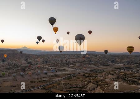 Kappadokien, Türkei - 14. September 2021: Weitwinkelaufnahme von bunten Heißluftballons, die am frühen Morgen bei Sonnenaufgang zusammen am Himmel schweben Stockfoto