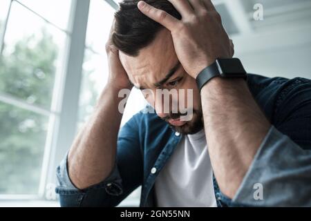 Sehr verärgert unglücklicher Mann, der an Kopfschmerzen, Schmerzen und Depressionen leidet, drückt Emotionen von Stress aus Stockfoto