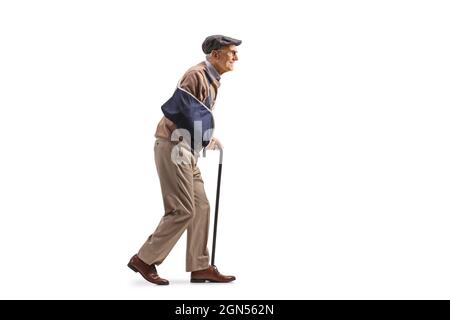 Ganzkörperaufnahme eines älteren Mannes mit einer Armschiene, der mit einem Gehstock auf weißem Hintergrund läuft Stockfoto