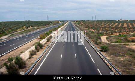 Luftaufnahme der modernen Autobahn Straße auf ländliche Landschaft außerhalb der Stadt. Zwei Wege Asphaltstraße mit Blick auf das Land in Andalusien mit verstreuten und niedrigen cl Stockfoto