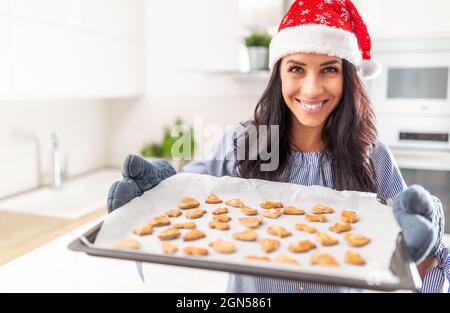 Schöne Bäckerin in weihnachtshut zeigt ihre Arbeit. Leckere Lebkuchen auf einem Backpapier. Stockfoto