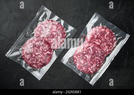 Beef Patties im Vakuumverpackungsset, auf schwarzem Steingrund, Draufsicht flach liegend Stockfoto