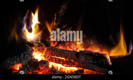 Heisses brüllendes Feuer und rote Kohlen in einem Kamin. Brennendes Holz in Schornstein und warme Atmosphäre im Winter. Helle Flamme des Feuers brennt Stockfoto