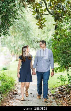Ein Paar in den Vierzigern, die Eltern sind, machen im Sommer einen Spaziergang in der Nachbarschaft auf dem Bürgersteig draußen Stockfoto