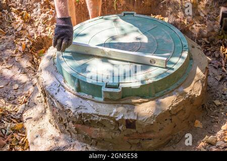 Installation eines Klärgruben mit einem Brunnen aus Betonringen. Ausrichten der Heckklappenabdeckung Stockfoto