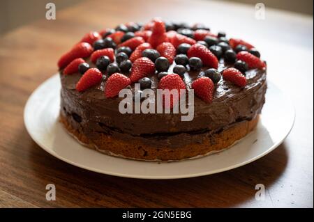 Schöne ganze hausgemachte vegane Schokoladenkuchen mit frischen Heidelbeeren und Erdbeeren dekoriert. Stockfoto