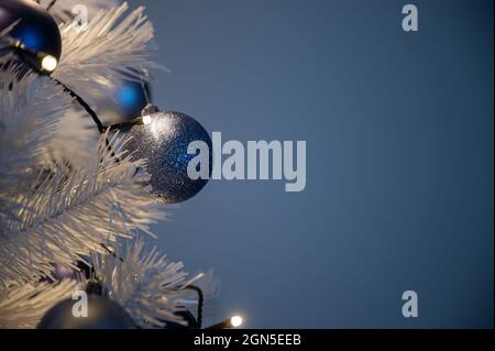 Festliches Bild von blauen weihnachtsblasen auf weißem Weihnachtsbaum mit Lichtern. Auf blauem Hintergrund mit Platz zum Kopieren für Ihren Text. Stockfoto