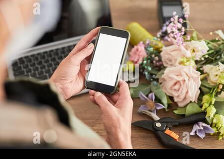 Nahaufnahme der weiblichen Inhaberin eines kleinen Unternehmens, die ein Smartphone mit leerem Bildschirm verwendet, während sie den Blumenladen verwaltet und Platz für Kopien verwendet Stockfoto