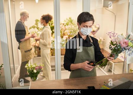 Portrait einer weiblichen Floristin, die Maske trägt, während sie Blumensträuße im Blumenladen arrangiert, Platz kopieren Stockfoto