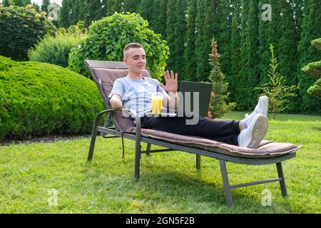 Ein Mann mit amputierten Armen trinkt einen Cocktail und spricht mit Freunden über einen Laptop Stockfoto