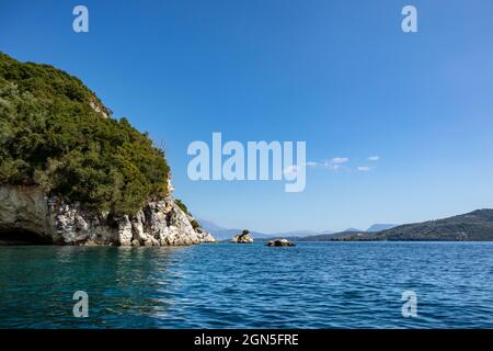 Blaues klares ruhiges Ionisches Meer in Ormos Desimi mit landschaftlich schöner, grüner Felsküste und hellem Himmel. Natur der Insel Lefkada in Griechenland. sommerurlaub id Stockfoto