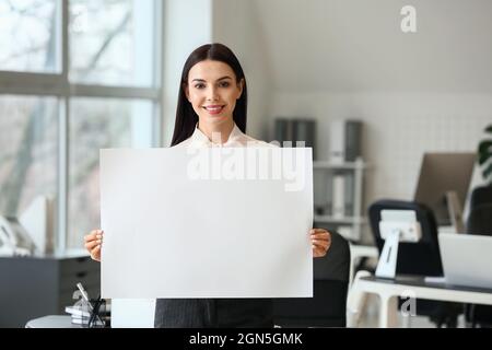 Junge Frau mit leerem Plakat im Büro Stockfoto