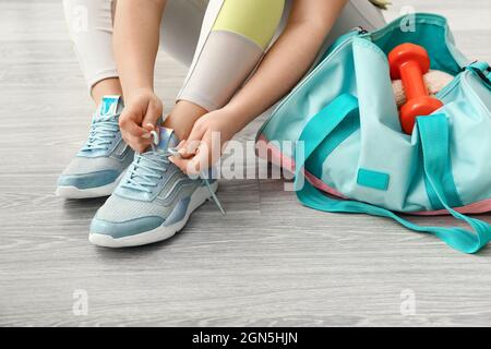 Frau, die Schnürsenkel und Tasche mit Hanteln auf hellem Holzboden bindet Stockfoto