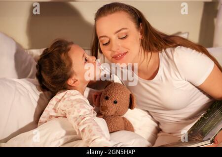 Kleines Mädchen, das ihre Mutter küsst, bevor es einschläft Stockfoto