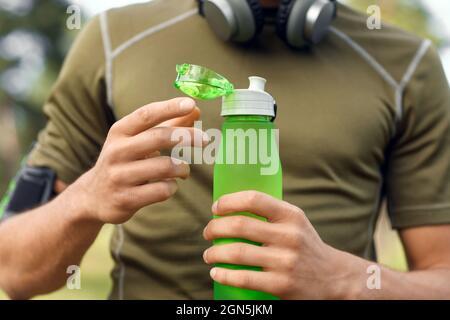 Sportlicher junger Mann, der eine Flasche Wasser im Park öffnet, Nahaufnahme Stockfoto