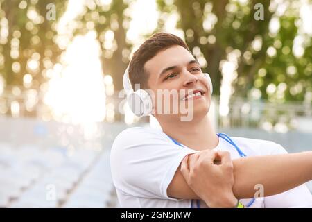 Sportlicher junger Mann mit Kopfhörern, der im Stadion trainiert Stockfoto