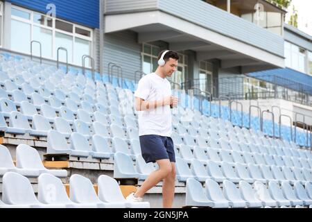 Sportlicher junger Mann mit Kopfhörern, der im Stadion unten läuft Stockfoto