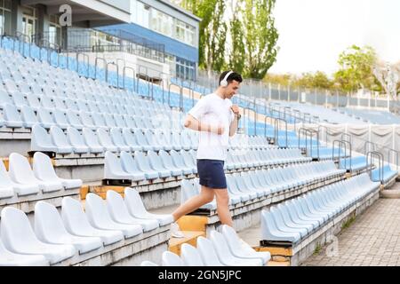 Sportlicher junger Mann mit Kopfhörern, der im Stadion unten läuft Stockfoto