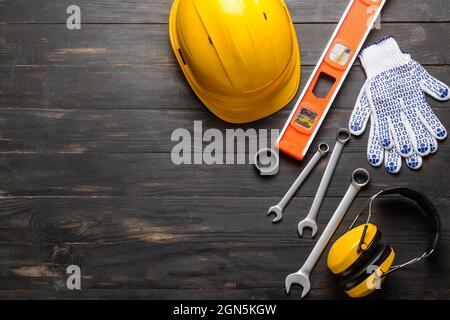 HardHat mit Baumaterial auf dunklem Holzhintergrund Stockfoto