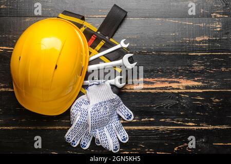 HardHat mit Baumaterial auf dunklem Holzhintergrund Stockfoto