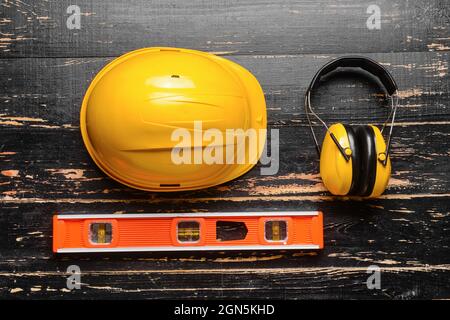 HardHat mit Ohrenschützern und Bauerniveau auf dunklem Holzhintergrund Stockfoto