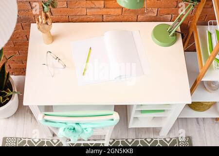 Komfortabler Arbeitsplatz mit Notizbuch, Bleistift, Brillen und Lampe auf dem Tisch in der Nähe der Ziegelwand Stockfoto