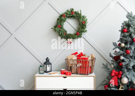 Adventskalender mit Geschenkschachteln im Korb, Kerzen auf Kommode und Weihnachtskranz an der Wand Stockfoto