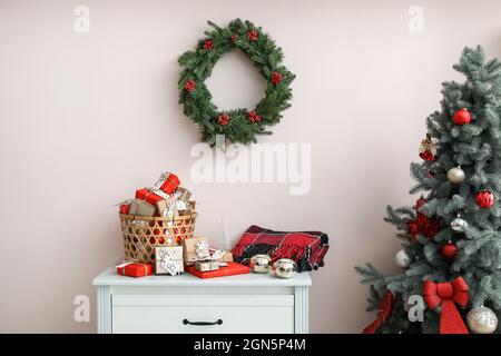 Adventskalender mit Geschenkschachteln im Korb, Kerzen, Plaid auf der Kommode und Weihnachtskranz an der farbigen Wand Stockfoto