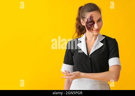 Frau, die zu Halloween als Zimmermädchen gekleidet war und etwas auf farbigem Hintergrund zeigte Stockfoto