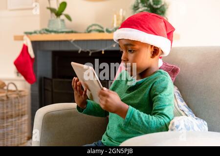 afroamerikanischer Junge mit Weihnachtsmütze und Tablet zur weihnachtszeit Stockfoto