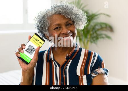 Glückliche ältere afroamerikanische Frau zeigt covid Impfstoff Pass auf dem Smartphone Stockfoto