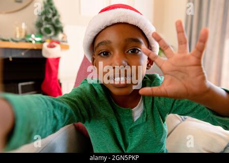 afroamerikanischer Junge mit Weihnachtsmütze, der zur weihnachtszeit einen Videoanruf abgibt Stockfoto