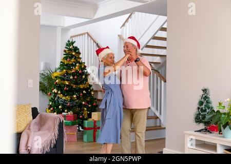 Glückliches kaukasisches Seniorenpaar mit Weihnachtsmütze, das zur weihnachtszeit tanzt Stockfoto
