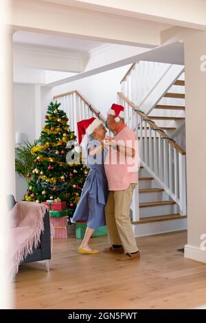 Glückliches kaukasisches Seniorenpaar mit Weihnachtsmütze, das zur weihnachtszeit tanzt Stockfoto